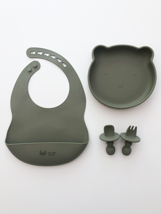 A silicone bib, bear plate, and baby utensil set (fork and spoon)  in a green sage colour. All the items are meant for use by babies or toddlers.