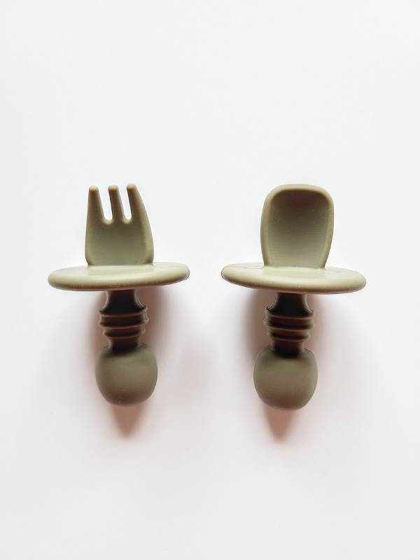 A green sage coloured silicone spoon and fork utensil set meant for toddlers. The utensils are short and stubby, with a shield to prevent toddlers from inserting the utensil too far into their mouth and gagging on it.  Edit alt text