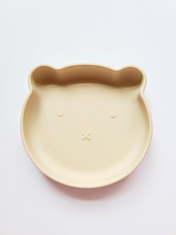 Wheat coloured silicone plate, with suction cup base, in the shape of a bear's face.