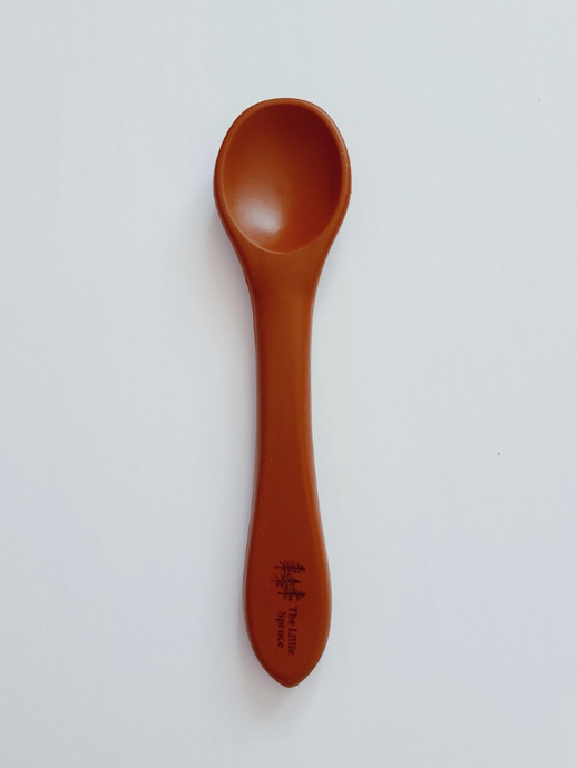 A small clay brown silicone spoon meant for use by babies and toddlers.