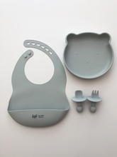 Load image into Gallery viewer, A silicone bib, bear plate, and baby utensil set (fork and spoon)  in a grey blue colour. All the items are meant for use by babies or toddlers.
