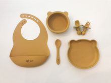 Load image into Gallery viewer, A silicone bib, spoon, bear plate, bear bowl, and baby utensils (fork and spoon) in a mustard yellow colour. All the items are meant for use by babies or toddlers.
