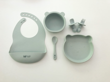 Load image into Gallery viewer, A silicone bib, spoon, bear plate, bear bowl, and baby utensils (fork and spoon) in a grey blue colour. All the items are meant for use by babies or toddlers.
