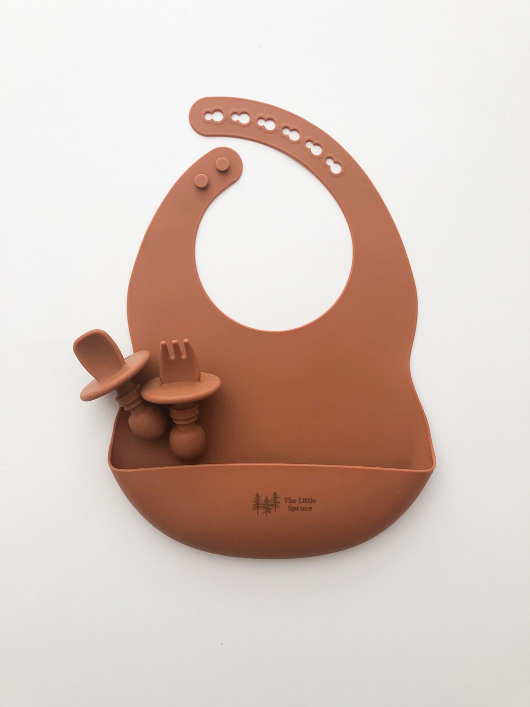A silicone bib, and baby utensils (fork and spoon) in a burnt orange colour. All the items are meant for use by babies or toddlers.