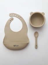 Load image into Gallery viewer, A silicone bib, bear bowl, and spoon in a beige sand colour. All the items are meant for use by babies or toddlers.
