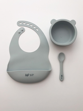 Load image into Gallery viewer, A silicone bib, bear bowl, and spoon in a grey blue colour. All the items are meant for use by babies or toddlers.
